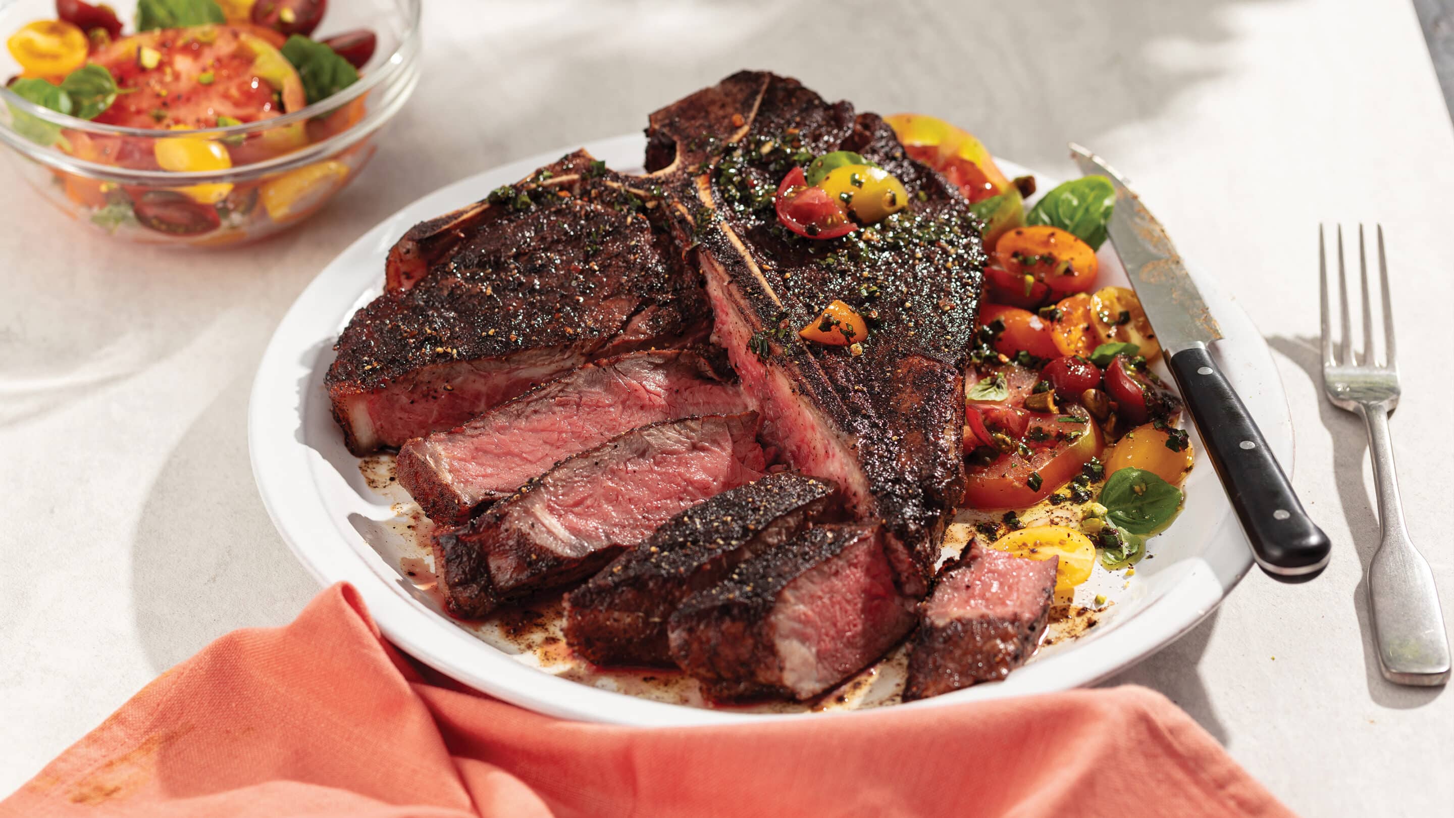 Smoked porterhouse steak with side of veggies on a white plate with light orange napkin underneath.