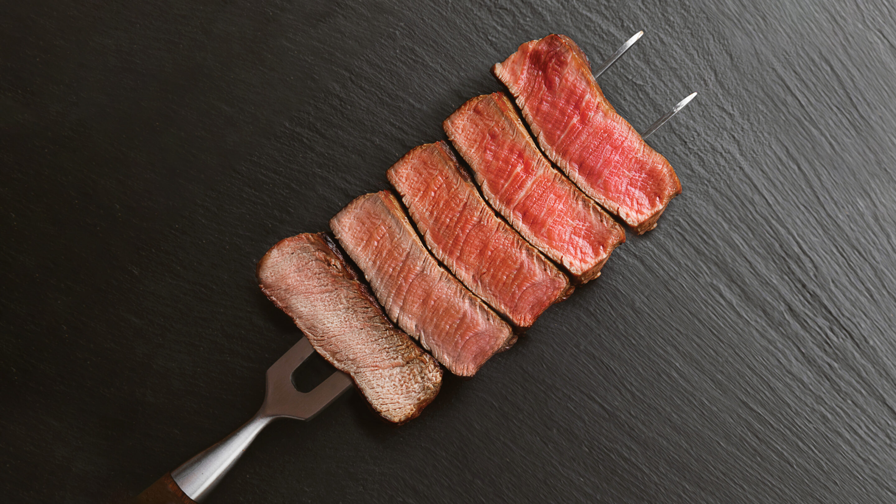 Chef holding white plate with cooked, sliced filet mignon served with a side of broccolini.