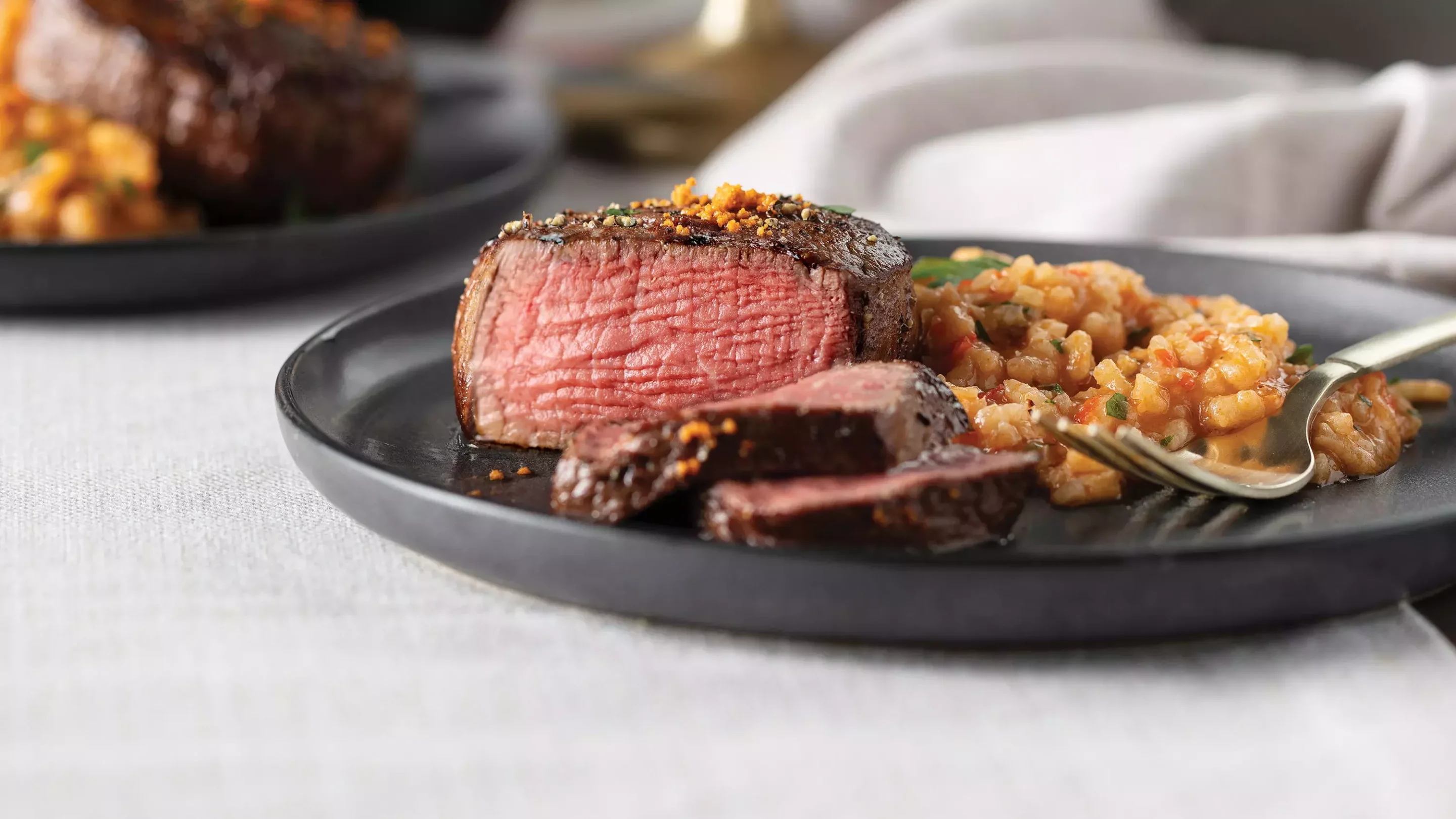 Chef holding white plate with cooked, sliced filet mignon served with a side of broccolini.