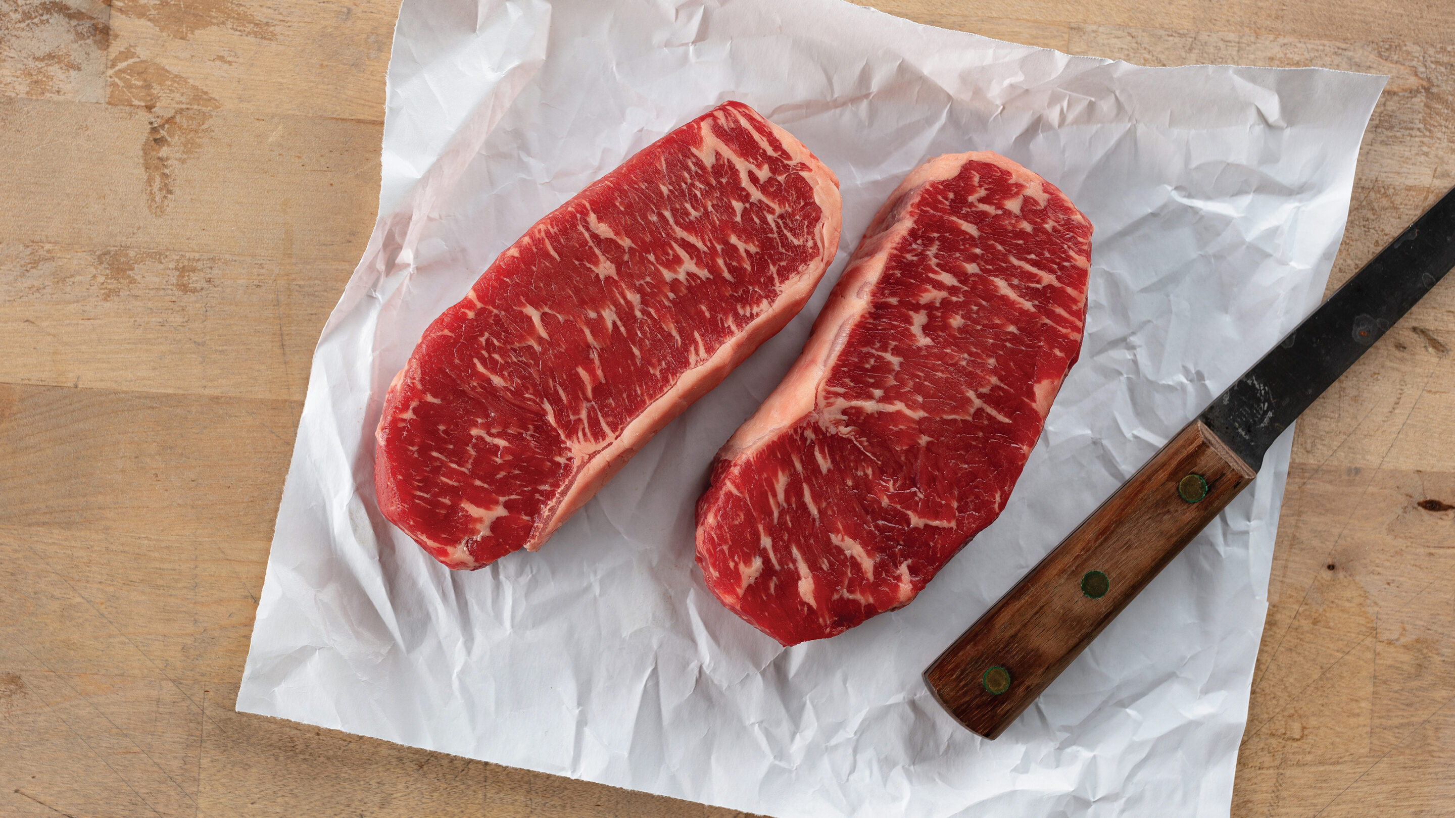 Chef holding white plate with cooked, sliced filet mignon served with a side of broccolini.