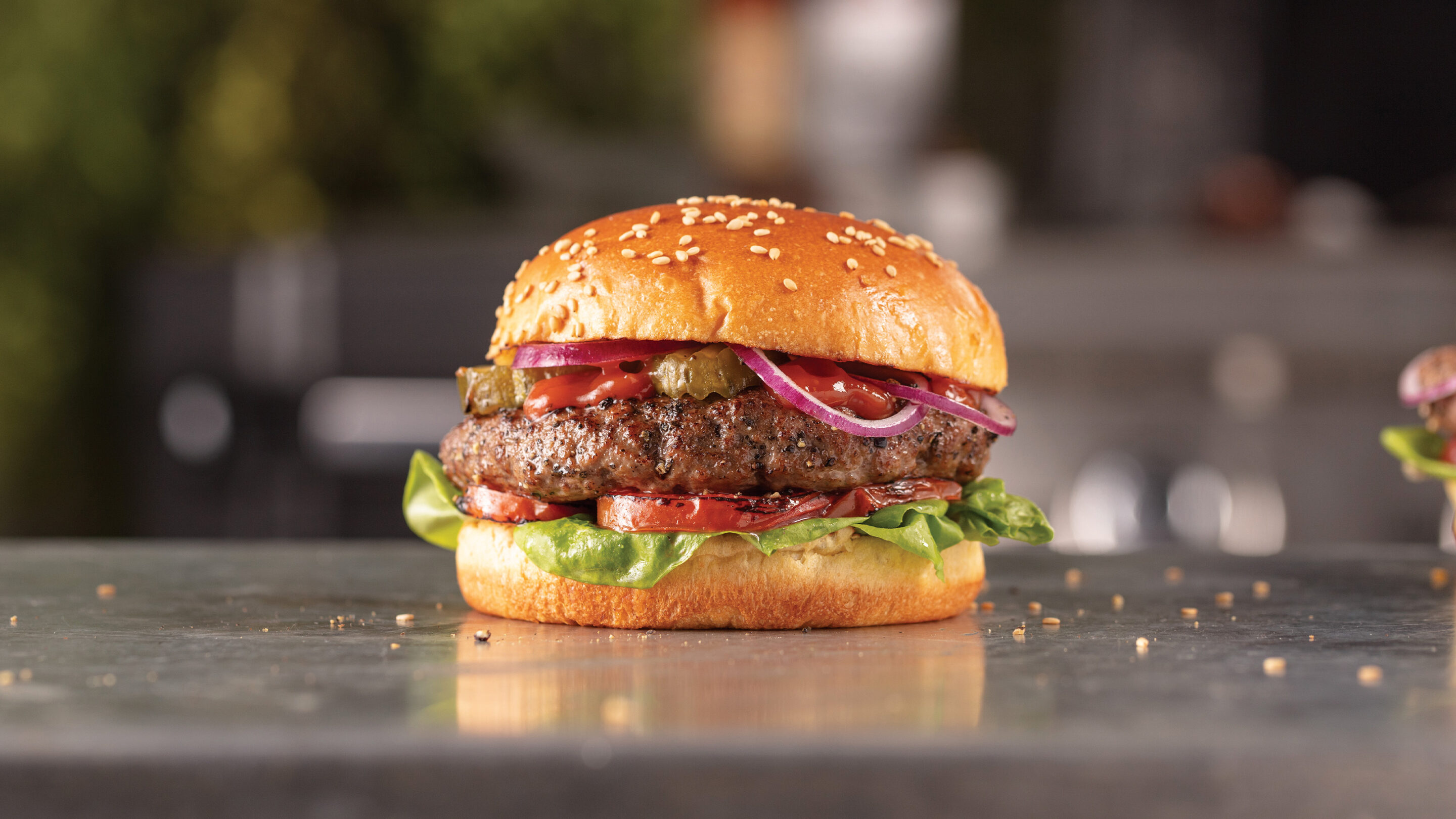 Person who holding hamburger with air fried burger, lettuce, tomato, pickles and red onion