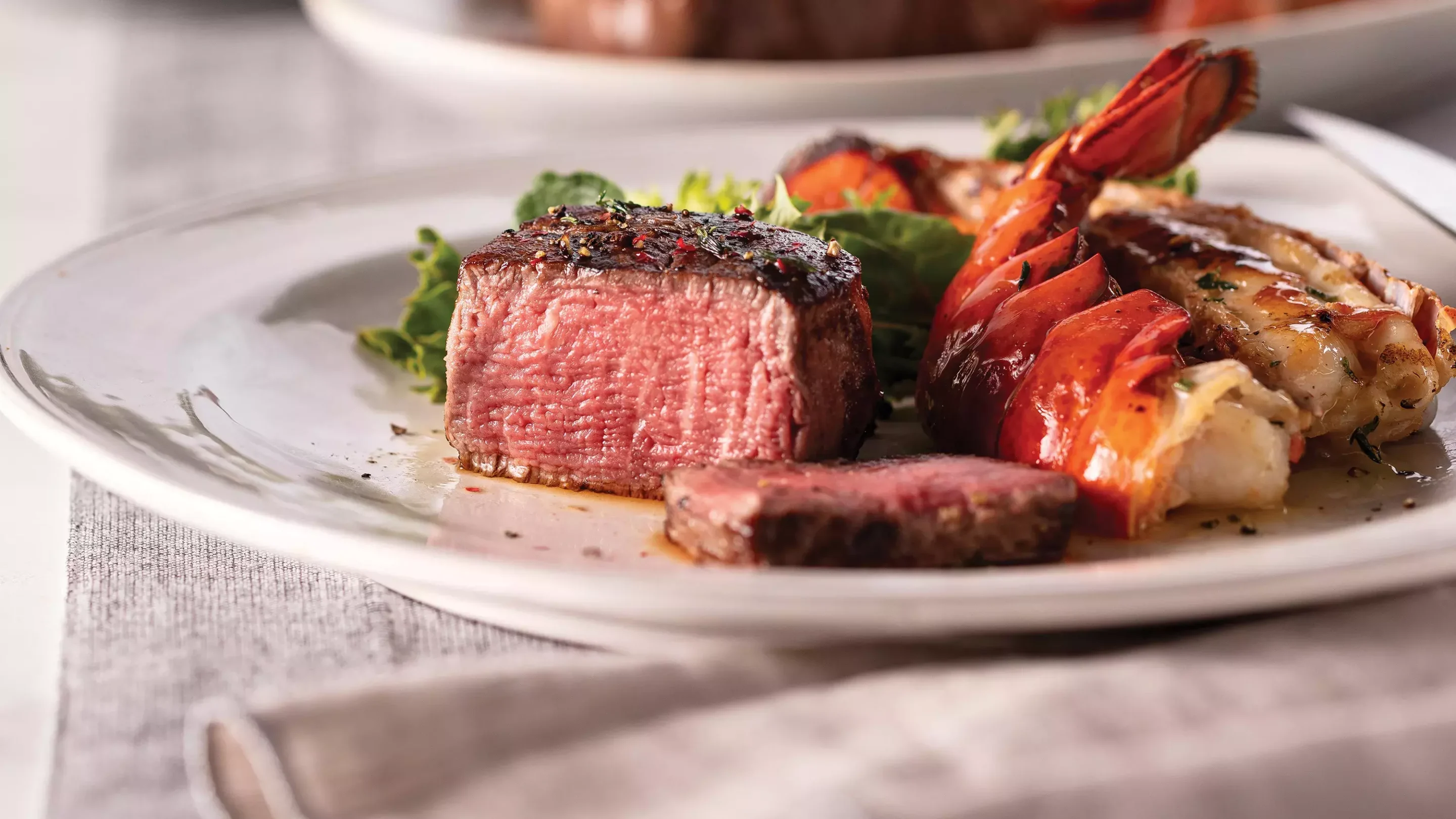 Chef holding white plate with cooked, sliced filet mignon served with a side of broccolini.