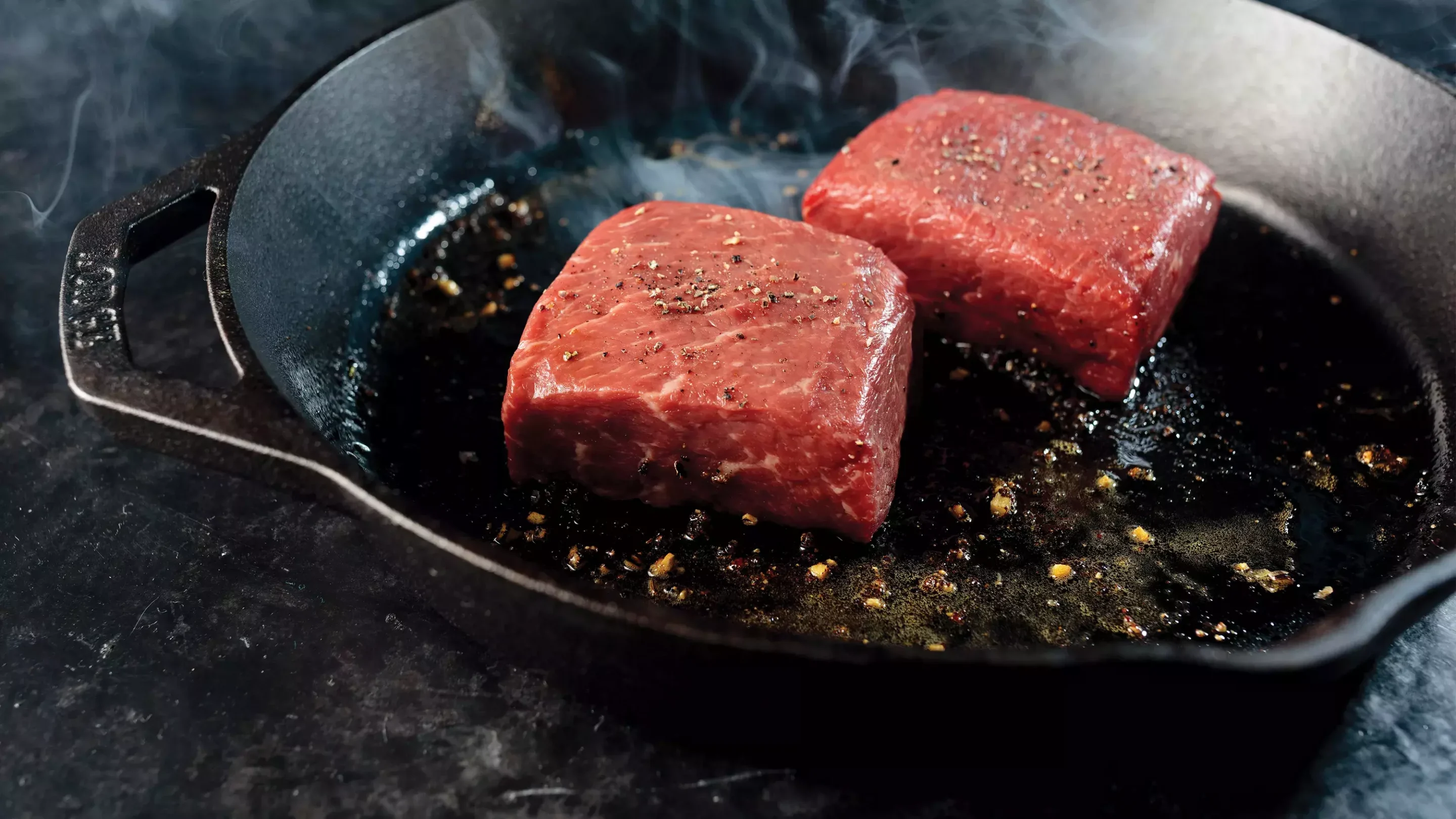 Seared King Cut New York strip steak in cast iron skillet with butter and garlic cloves on a gas stove.