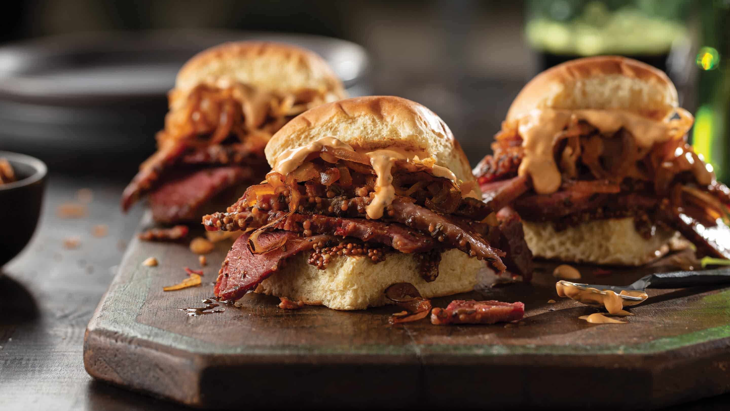 Three corned beef sliders with beer cheese sauce on a platter