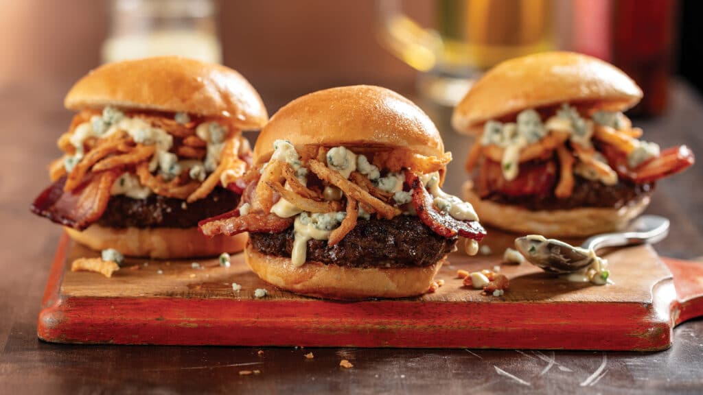 3 Bacon black 'n blue cheese sliders with crispy onion straws on a platter.