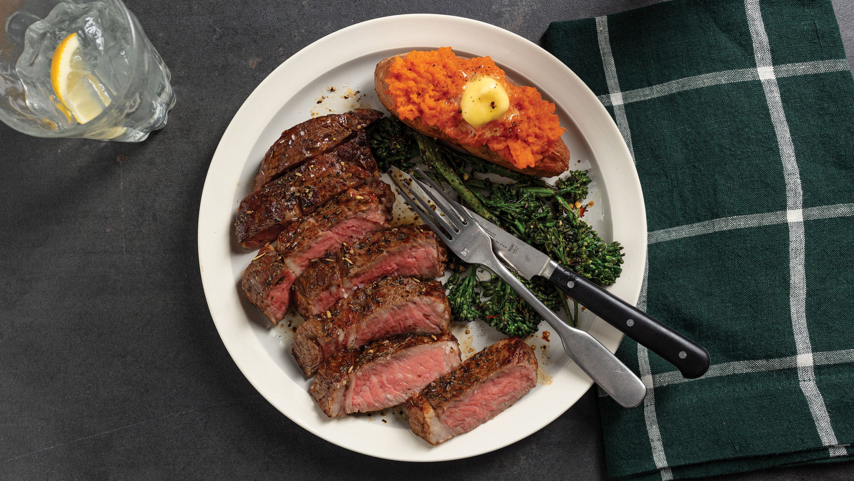 White plate with sliced medium-rare pan-seared ribeye, roasted broccoli and sweet potato.