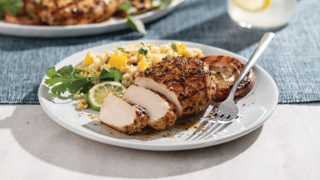 Grilled chicken breast with rice on white plate with blue napkin.