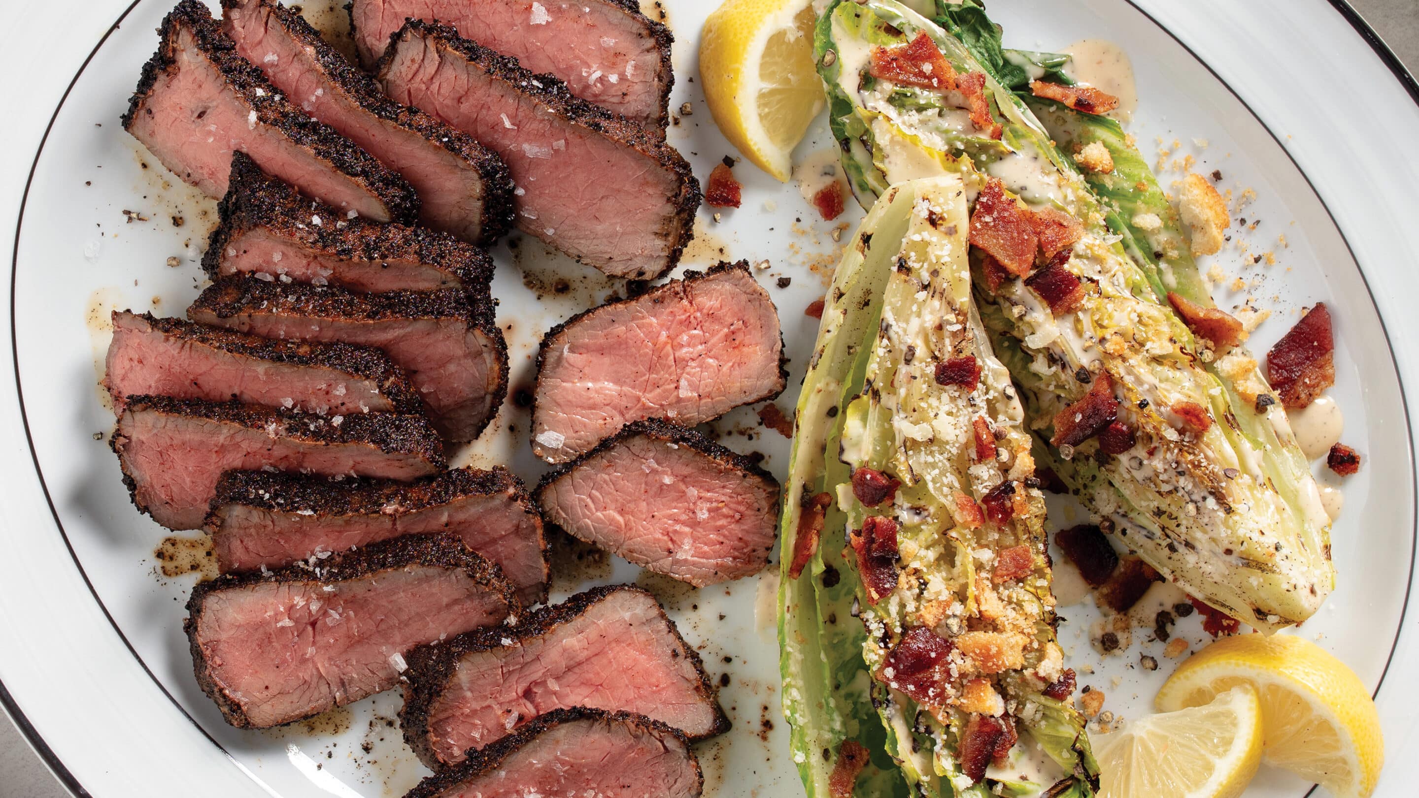 Ancho-coffee top sirloin cooked medium-rare and sliced with side of grilled caesar salad on a white plate