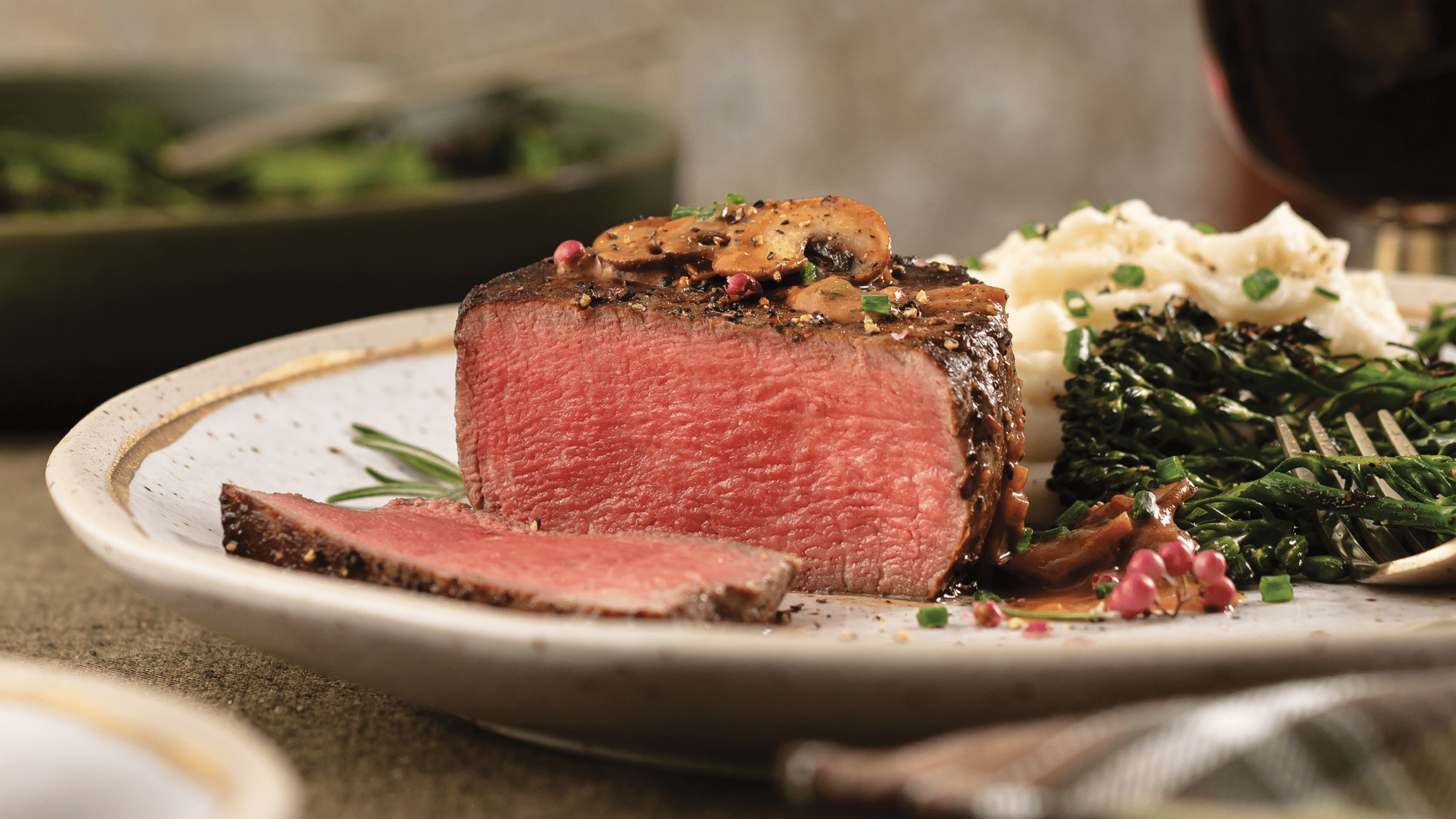 Filet Mignon cooked medium-rare with mushroom sauce served with garlic mashed potatoes and broccolini on a white plate.