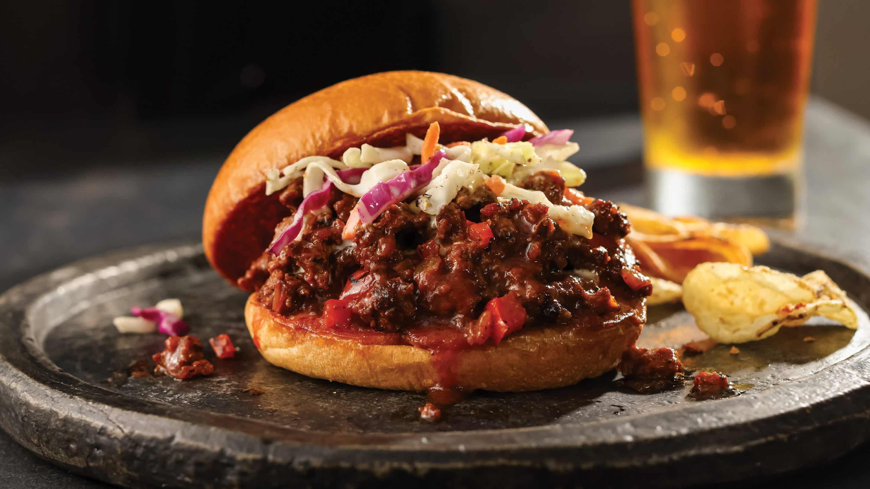 BBQ sloppy joe and chips on a silver plate served with a beer.