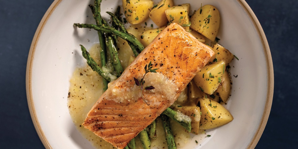 Broiled Salmon With Asparagus, Buttered Potatoes, and White Wine & Lemon Butter Finishing Sauce on a white plate