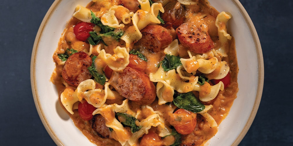 Grilled Kielbasa With Spinach, Tomatoes, Noodles, and Creamy Tomato & White Wine Finishing Sauce on a white bowl