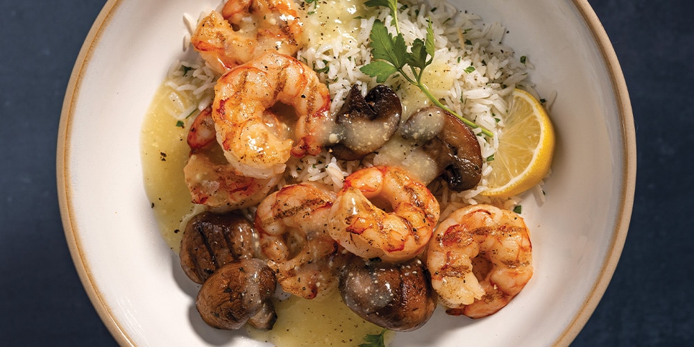 Grilled Shrimp and Mushrooms With Rice and White Wine & Lemon Butter Finishing Sauce on a white plate