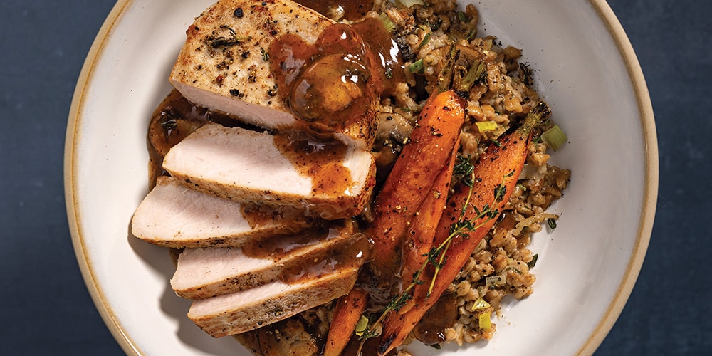 Pan-Fried Pork Chops on a white plate With Farro Risotto, Honey Carrots, and Red Wine & Mushroom Finishing Sauce 