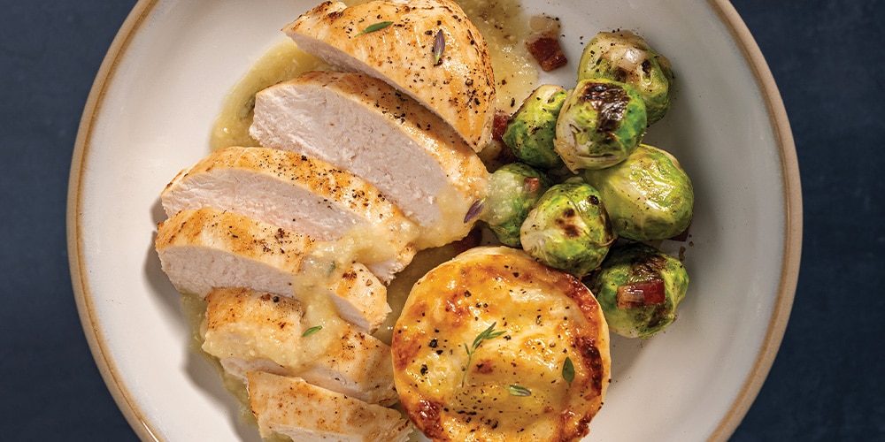 Pan-Seared Chicken Breasts, Scalloped Potatoes, Brussels Sprouts, and White Wine & Lemon Butter Finishing Sauce on a white plate