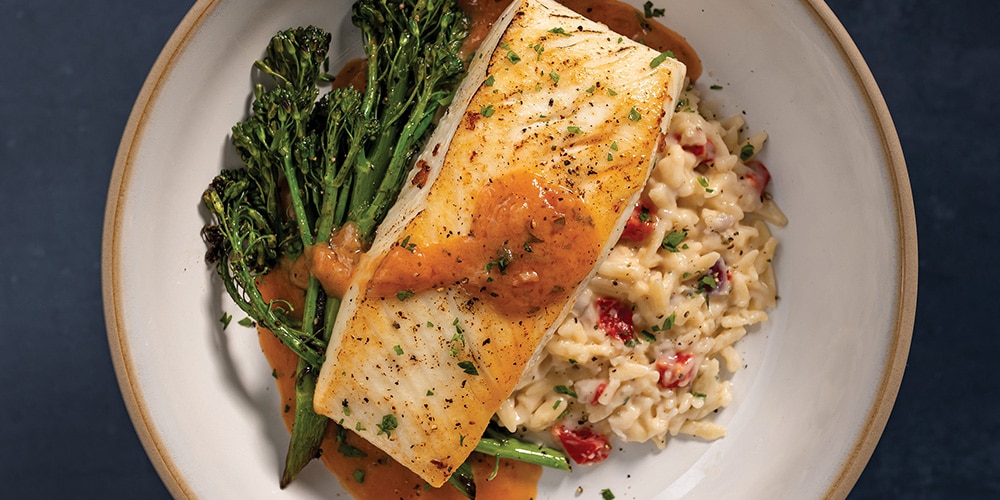 Pan-Seared Halibut With Creamy Orzo, Butter Broccolini, and Creamy Tomato & White Wine Finishing Sauce on a white plate