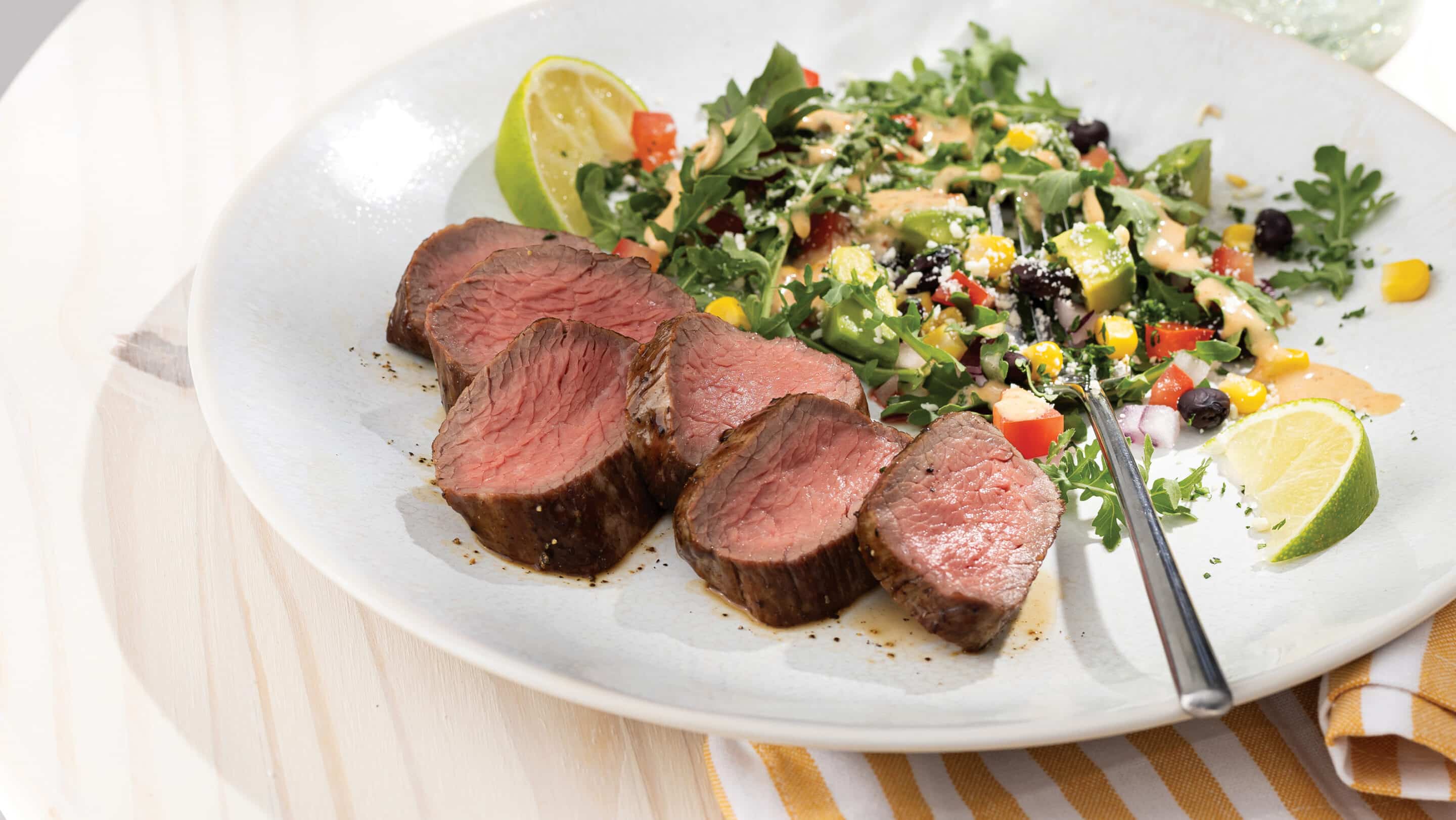 White plate with slices of bistro steak cooked medium-rare served with a southwest salad.